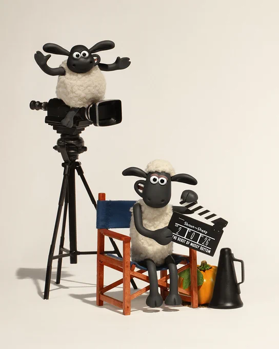 Shaun the Sheep and Timmy setting up a film scene, with one character behind a camera on a tripod and the other holding a clapperboard, surrounded by film equipment.