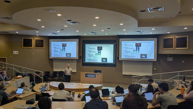 A lecture at NASA Ames, with a presenter speaking in front of two projected screens in an auditorium filled with attendees.