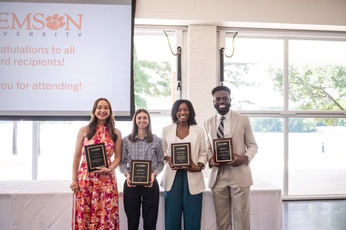 Four students posing for a photo holding awards.
