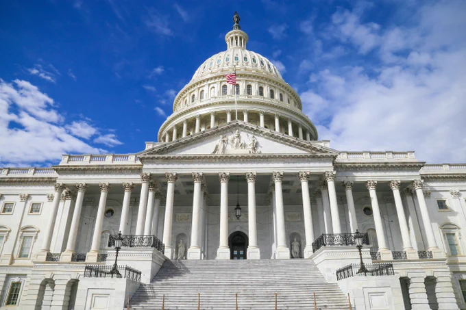 a low-angle photo of the U.S. Capitol building, with a blue sky overhead