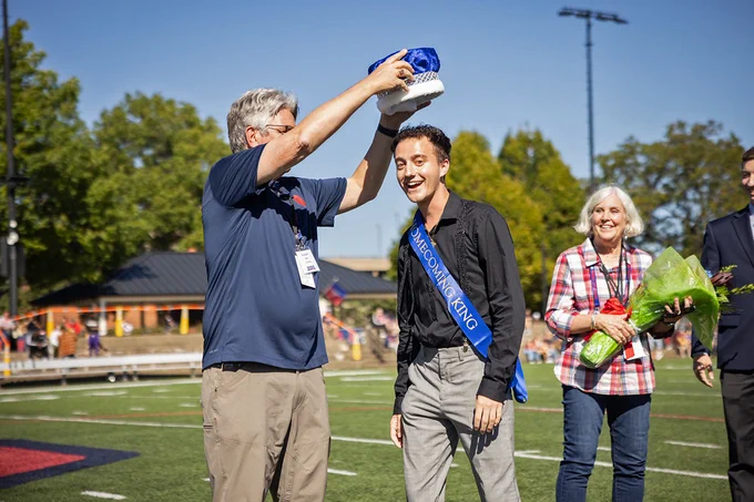 Duquesne President Ken Gormley places the Homecoming King crown on Braden Niles' head at Rooney Field during halftime of the football game. Laura Gormley is at right holding a bouquet of flowers.