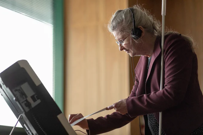 Photo of a blind woman with a white cane, sliding her ballot in a ballot marking device.