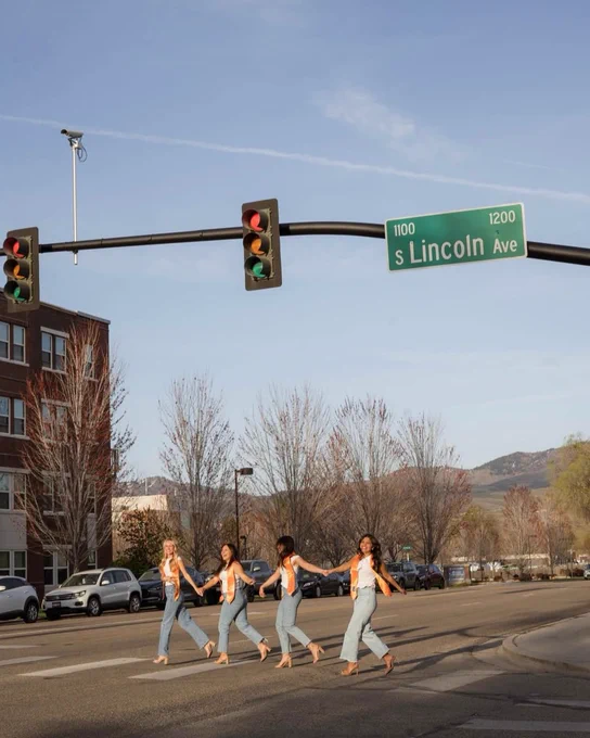 Four Boise State undergraduate students wearing graduation stoles and walking across Lincoln Avenue.
