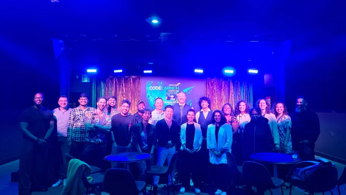 Group photo of diverse individuals at a "Code Launch Canada" event, standing on a stage lit with blue and purple lights. Ready to pitch their starup at our equity free accelerator