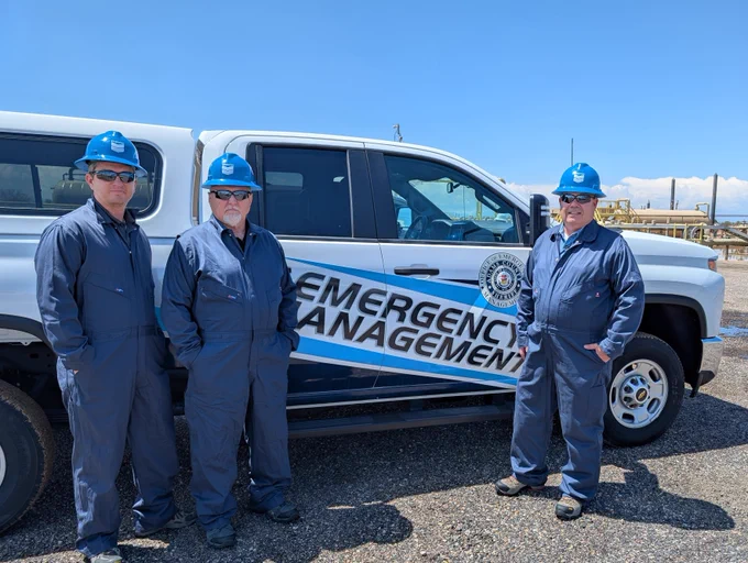 Members of Adams County Office of Emergency Management stand by their truck in protective gear to tour a Chevron oil and gas facility.