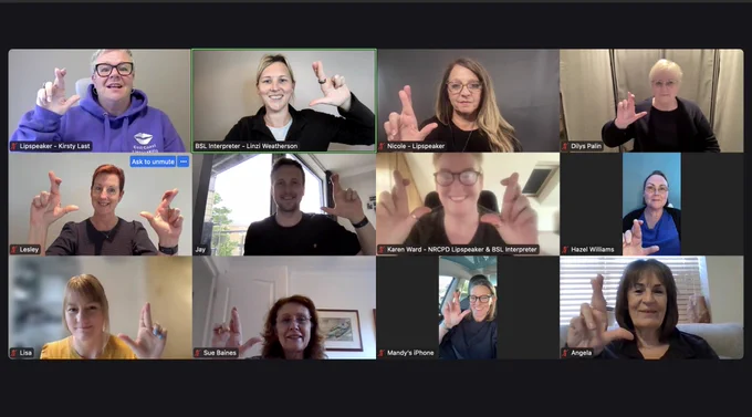 12 people in an online meeting, all showing the British Sign Language sign with their right hand for ‘Lottery’