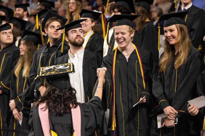 Graduates in caps and gowns smiling and celebrating during a graduation ceremony.