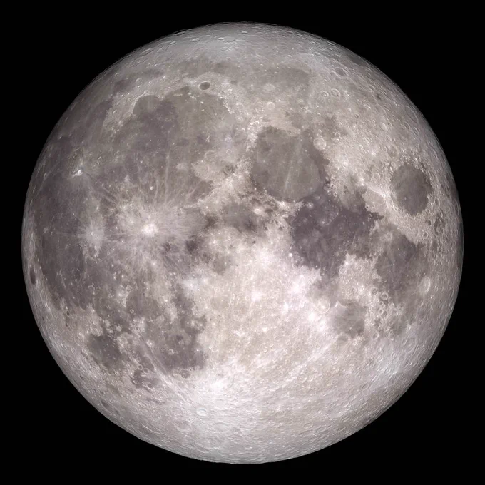 The Moon is a dark gray and white globe, with patches of darker white mottling its surface. Bright white impact craters dot the surface, with white spokes extending out from them.