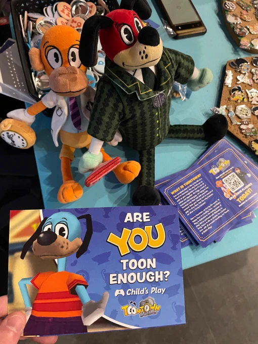 A infocard featuring Flippy Doggenbottom from Toontown Rewritten shows text reading “Are YOU Toon Enough?” With the Child’s Play logo above the Toontown Rewritten logo. The backside can be seen below that gives a description of the game and plushie campaign—plus a QR code and link to the Makeship page. Above the cards lie the Doctor Surlee and Lord Lowden Clear plushies!