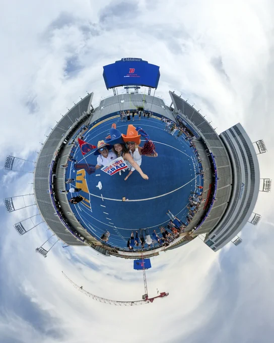 A tiny planet photo of Boise State graduates with friends and family on the blue turf inside Albertsons Stadium.
