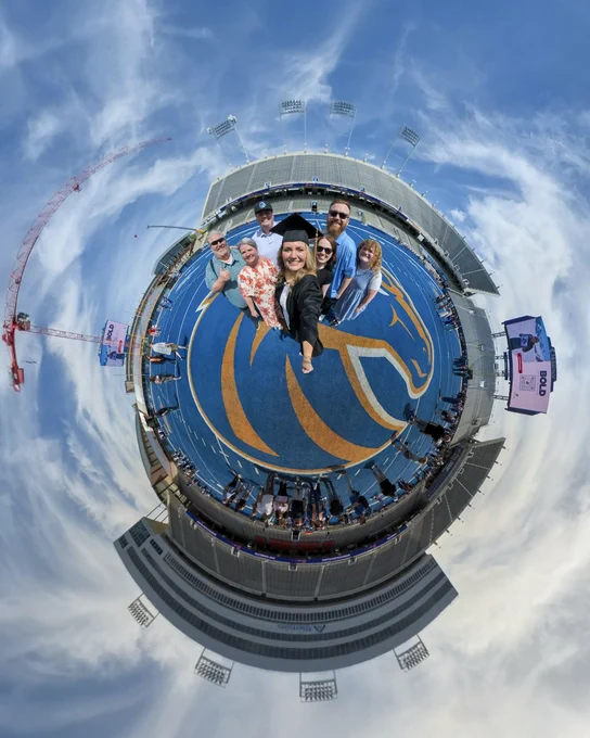 A tiny planet photo of Boise State graduates with friends and family on the blue turf inside Albertsons Stadium.