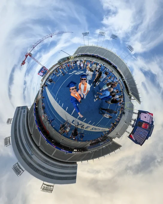 A tiny planet photo of Boise State graduates with friends and family on the blue turf inside Albertsons Stadium.