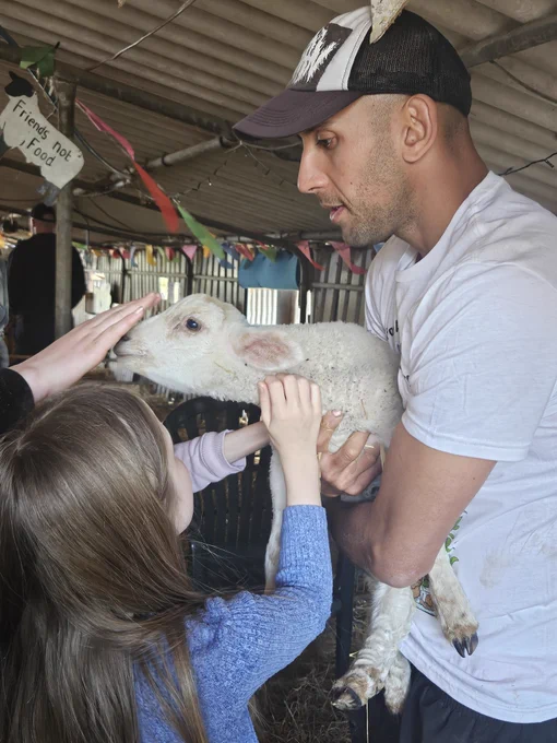 A sanctuary carer holds a little lamb as young people reach out to touch them