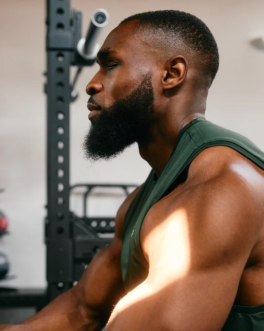 A left side-profile image of Michael, a black man. He is wearing a green tank top and there is gym equipment in the background.