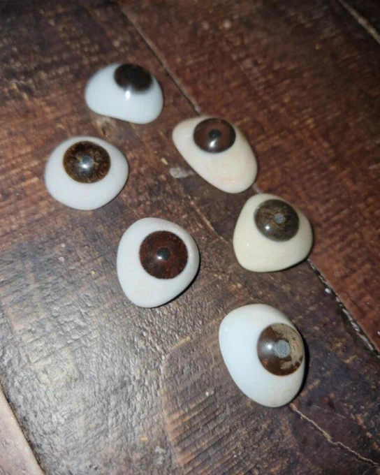 Image of six prosthetic eyes on a wooden table.