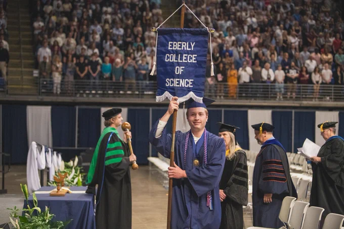 Student marshal Nate Carey carrying the Eberly College of Science flag at commencement.