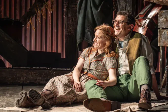 A photo showing two performers in vintage rustic outfits sat together on a stage 