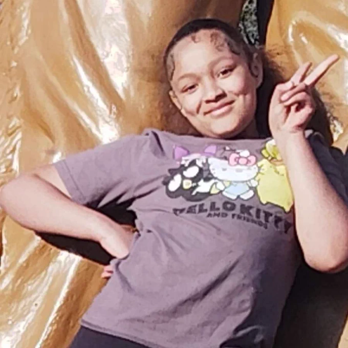 Person in a Hello Kitty t-shirt leaning on a large sculpture, making a peace sign with their hand.