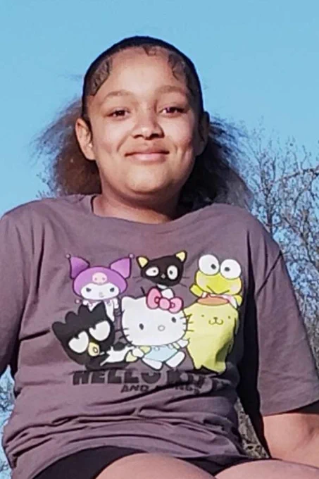 Person sitting on stone steps outdoors, wearing a t-shirt with "Hello Kitty and Friends" characters.