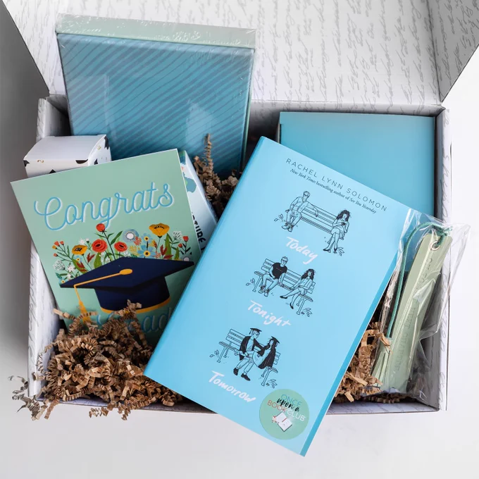 An open box with a hardcover copy of Today Tonight Tomorrow next to a Congrats card and other themed gifts wrapped in blues and greens