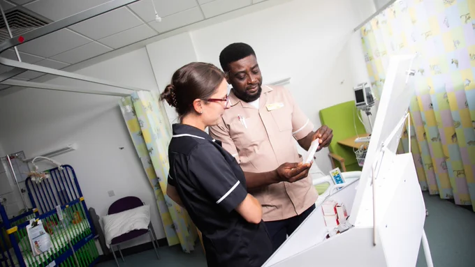 Nursing apprentice examining medications on a ward, supported by a tutor