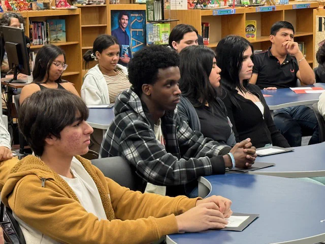 Students sit at tables and listen.