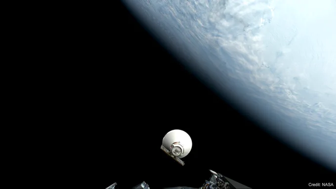 NASA’s SPHEREx observatory separates from its spacecraft after launch on March 11, 2025. The pale blue marble of Earth fills the upper right, its surface coated in clouds. A circular base with a flat, rectangular solar panel attached to it faces the camera. A large white cone extends from that, its opening facing the darkness of space. Metal hardware along the bottom edge of the image shows the portion of the launch vehicle that carried SPHEREx to orbit, where the camera is mounted. The image is watermarked “Credit: NASA.”