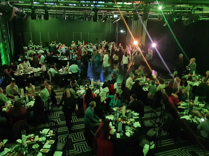 People dancing on the dance floor in the centre of the room filled with round tables. 