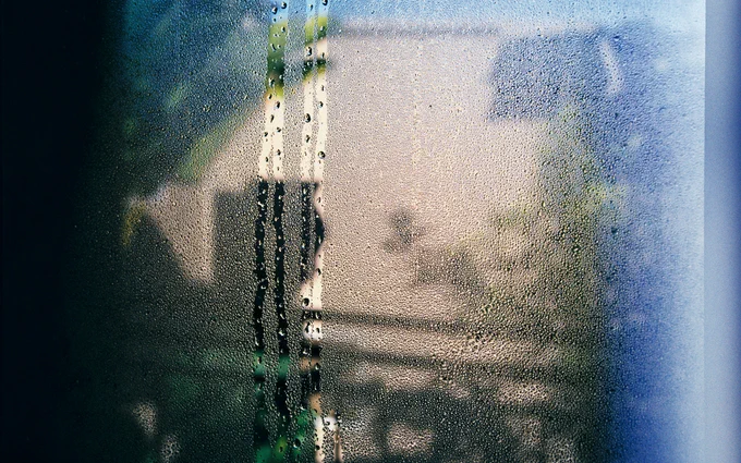 Condensation and streaks of water on a window, with blurry view of a city street in the background.
