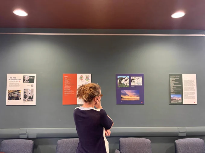 A woman is looking at four panels of artwork and prose on a wall above seating in howe library