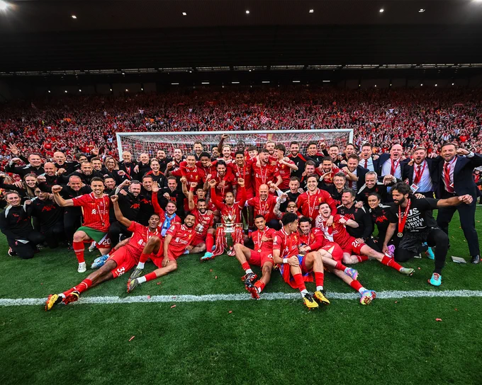 Photography of the Liverpool team with the Premier League trophy in front of the Kop.