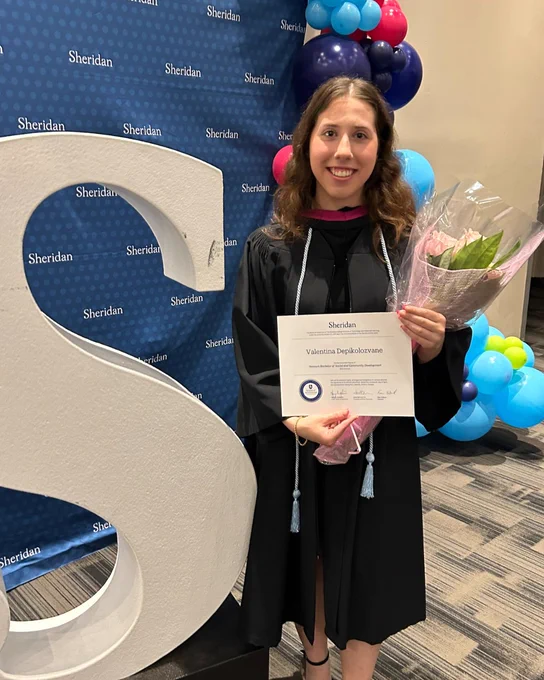 Valentina Depikolozvane stands beside the Sheridan 'S' at Convocation while holding her degree