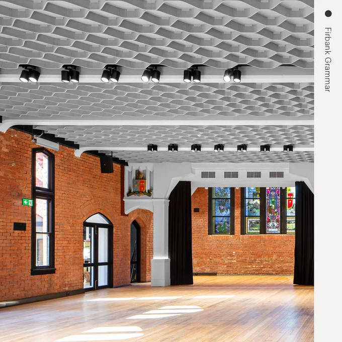 Interior of historic school building featuring a modern ceiling design, exposed brick walls, elegant black columns, and stained-glass windows.