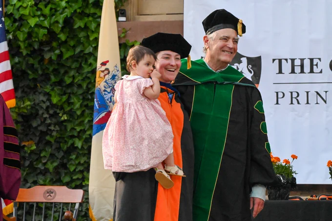 Professor Dan Notterman stands with a newly hooded PhD student who is holding a young child
