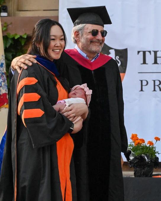 a newly hooded grad holds a newborn