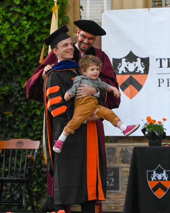 a PhD student is hooded while holding a toddler