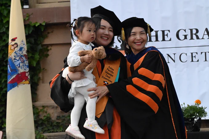a newly hooded grad student poses for a photo while holding a young child