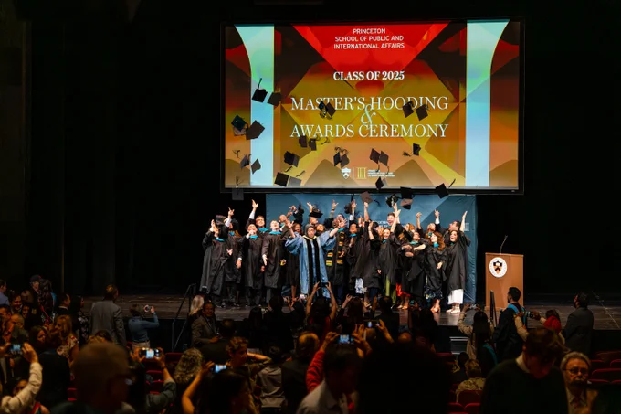 A group of individuals on stage in graduation attire throwing their hats in the air