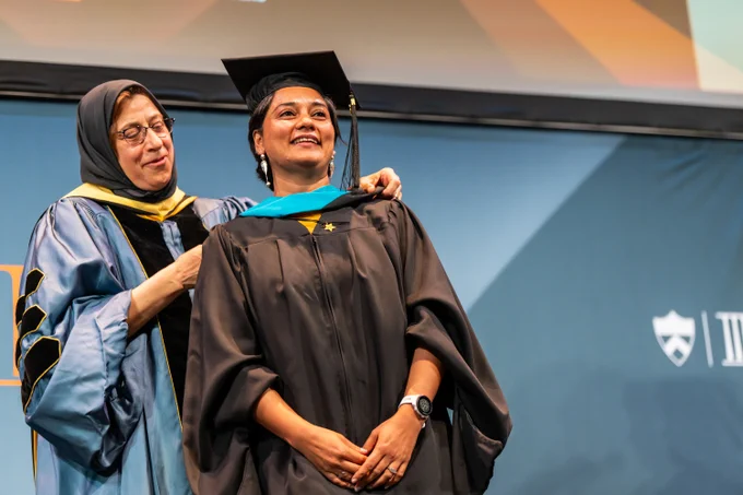 An individual receiving her graduate hood during a ceremony
