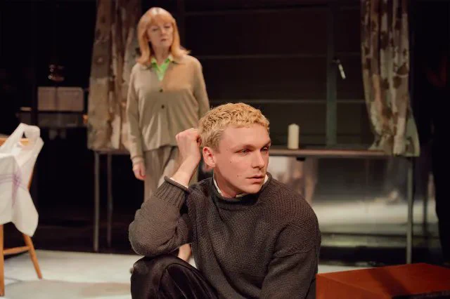 A photo showing two individuals in casual attire on a naturalistic stage setting 