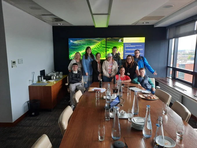 A group of TCPID students and staff with colleagues from EY in a meeting room with a large screen behind them, 