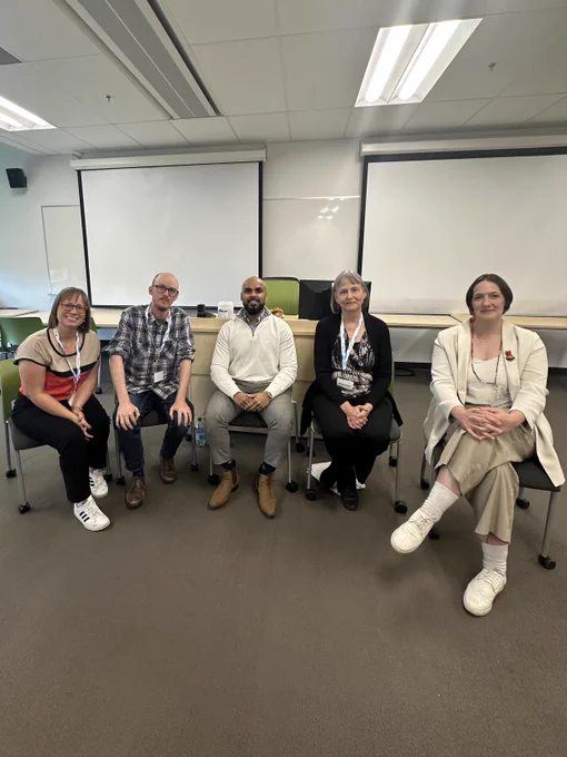 5 people sitting at a panel smiling and posing for a photo.
