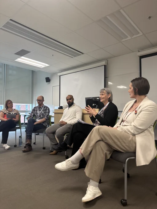 5 people sitting at a panel discussing with the audience. 
