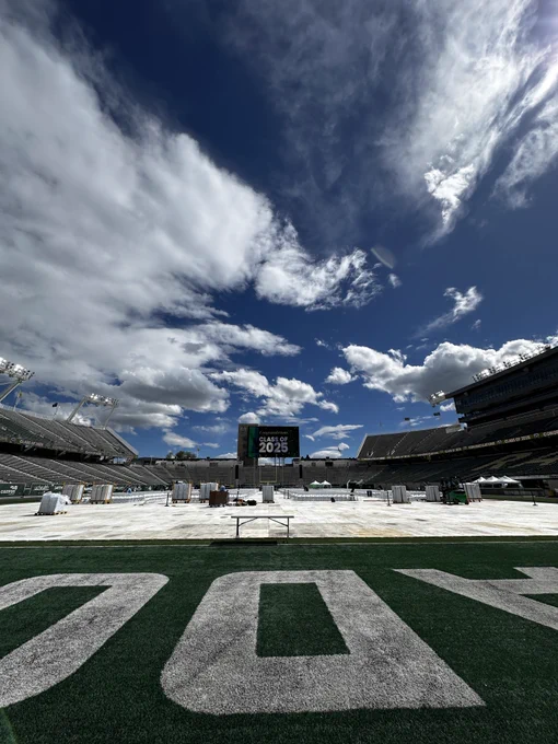 The field at Canvas Stadium. Staging is happening for Commencement and the big video screen has a graphic on it that says, "Congratulations, Class of 2025." 