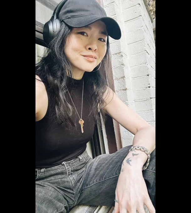 Ruibo Qian sitting with a black hat and shirt, and jeans. Key hanging from her neck