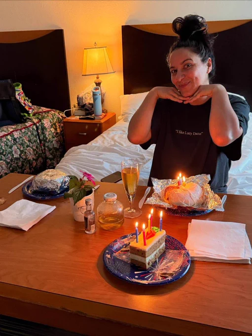 Madelein Sami in a hotel room eating what looks like cake  and a shirt that says I like Lucy Dacus