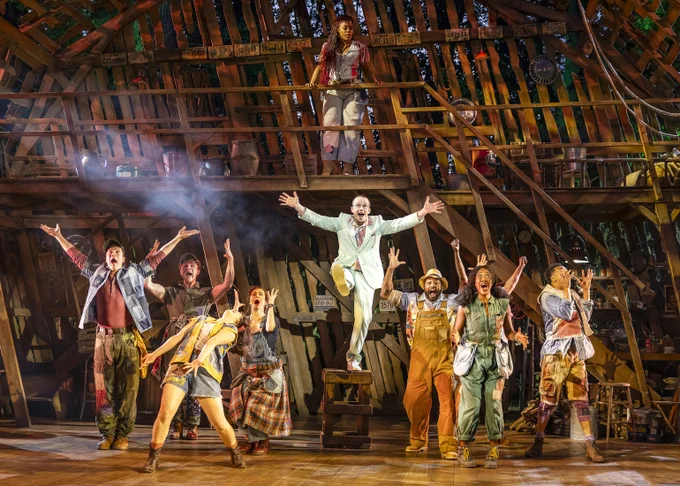 The company of Shucked celebrate in excitement, with Gordy (performed by Matthew Season-Young) with raised arms in the middle.