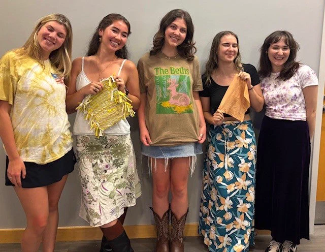 Five students hold and wear the shirts and sewing projects they created