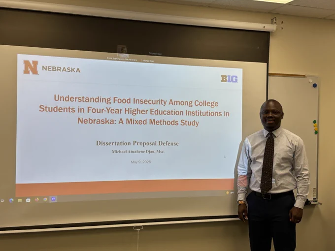 person standing beside a projection screen with research proposal title page