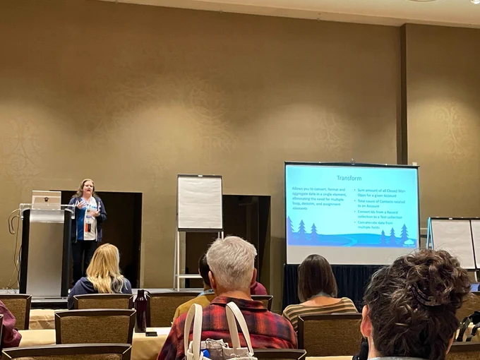 An attendee gives a presentation from a podium in a conference room at Tahoe Dreamin’. The audience is seated, facing a screen that displays a slide titled "Transform" with Salesforce-related content.

